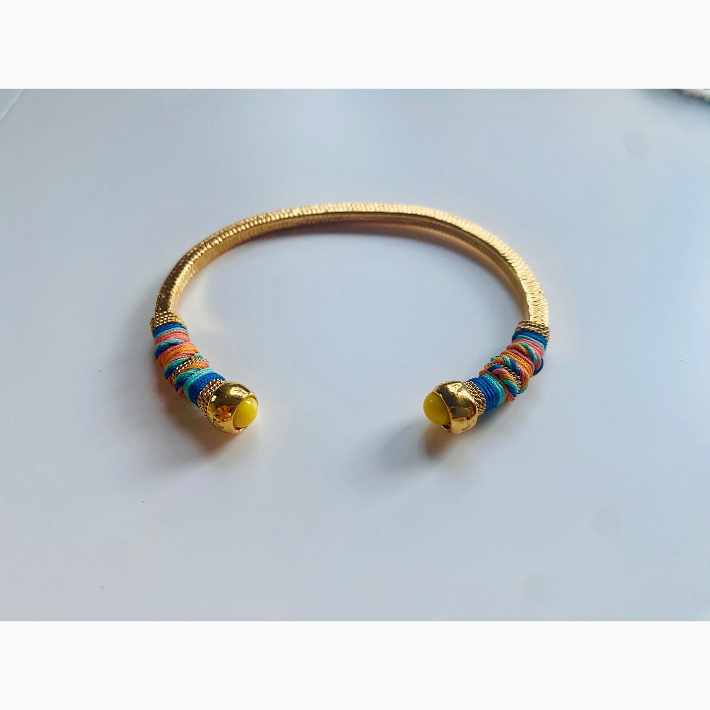Gold plated bracelet embellished with tinted threads and gold plated chains. The bracelet is adorned with glass beads at ends. Adjustable size. Product Details Yellow Gold Plated Cotton Rope or all metal Width: 0,6 cm; Circumference: 14,5 cm